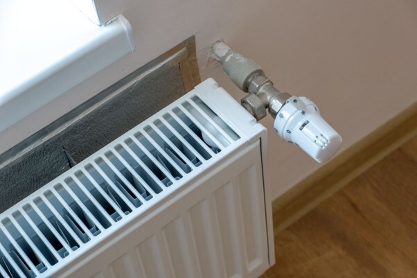 Signs your heating system needs power flushing, illustrated by a central heating radiator with a thermostatic radiator valve and connected pipework.