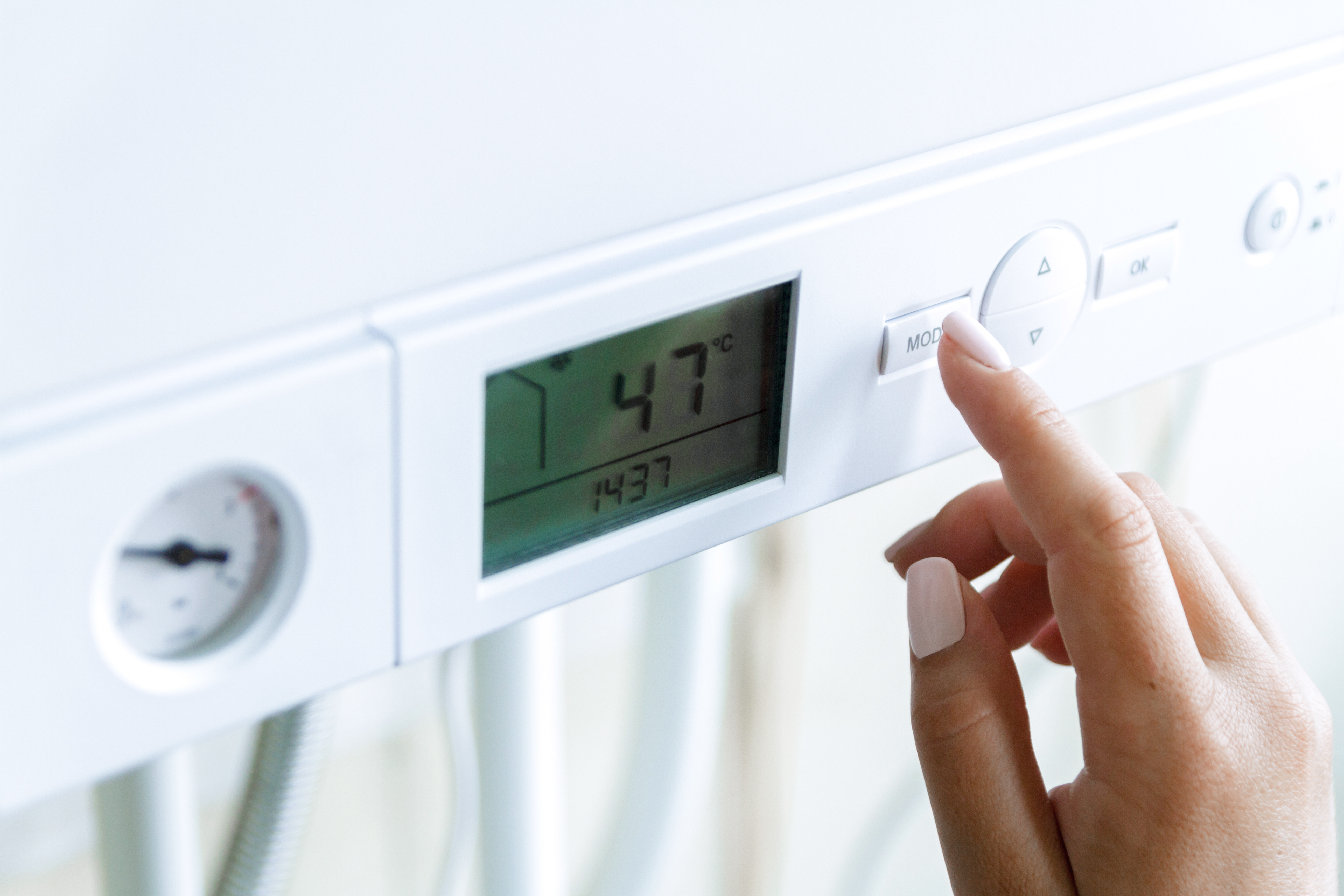 A homeowner’s hand adjusting the temperature settings on a modern boiler while wondering about the most common boiler problems.