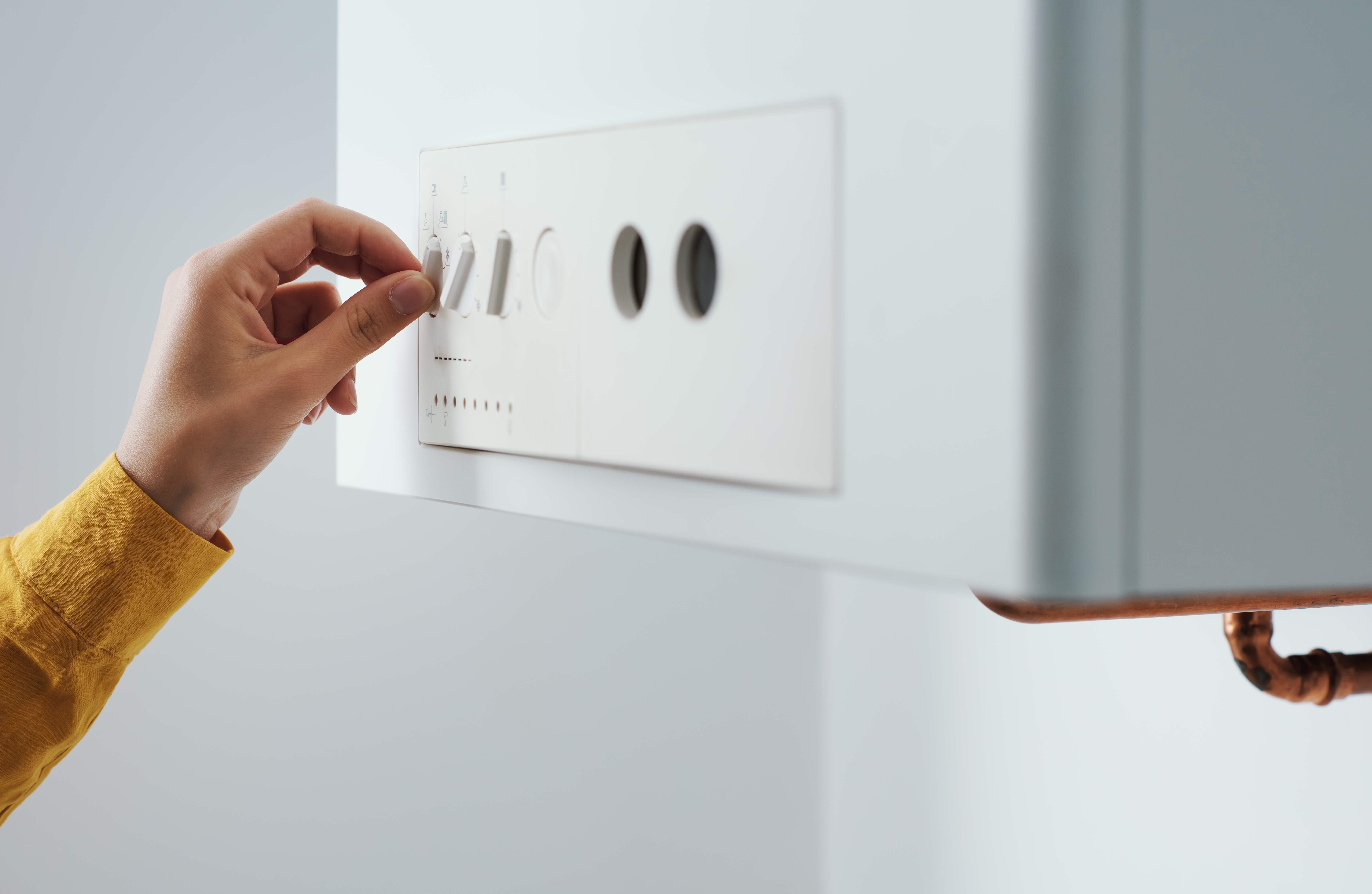 A homeowner’s hand adjusting the settings on a domestic boiler in their home, showing the difference between combi boiler and regular boiler.